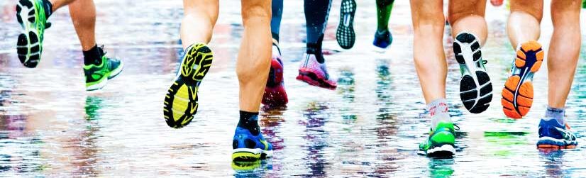 Runners moving across wet pavement in colorful gear during a rainy run